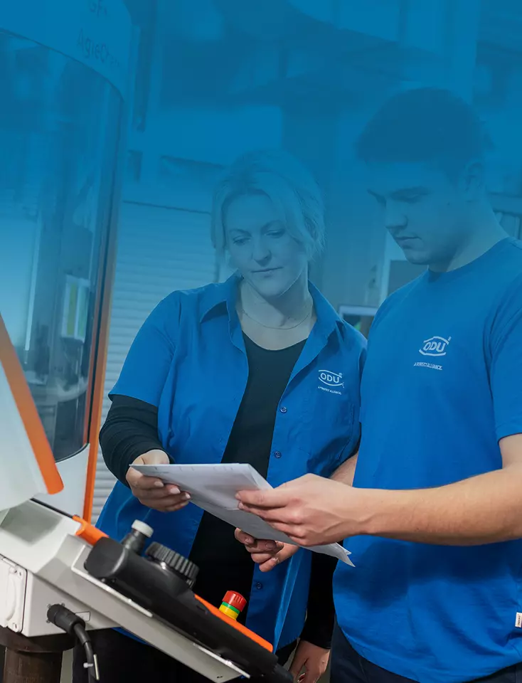 Two ODU employees look at a plan in front of a machine.