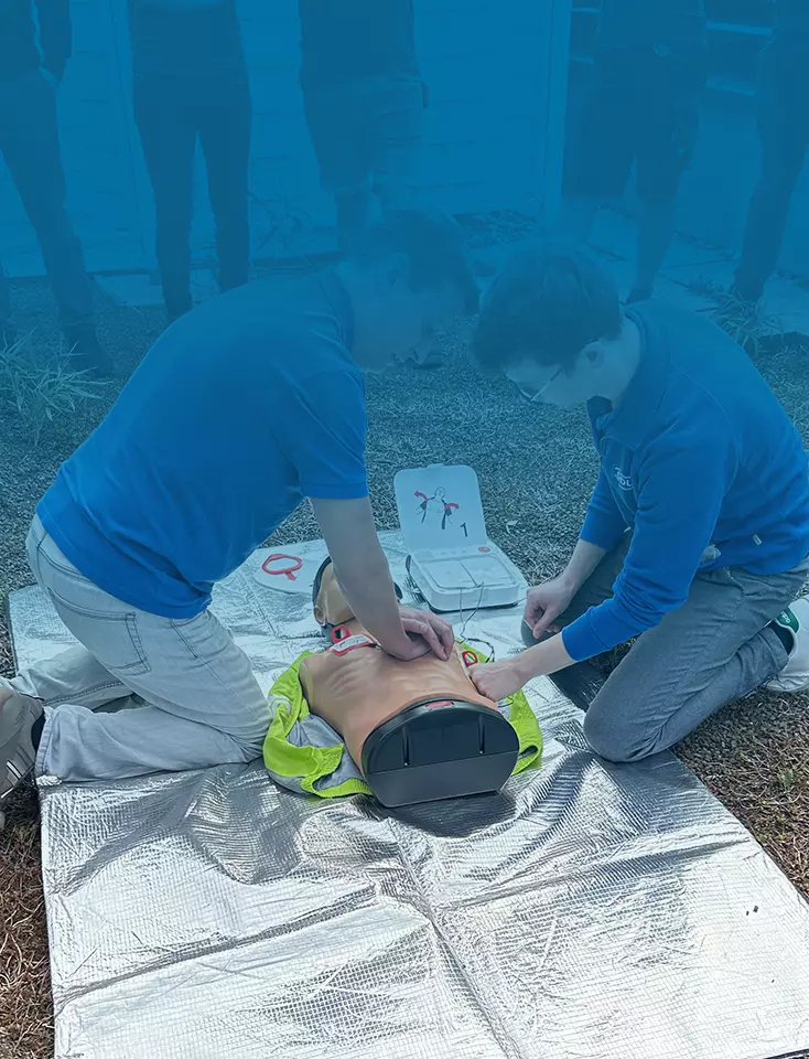 Two ODU employees kneel on the floor and practice chest compressions on a dummy.