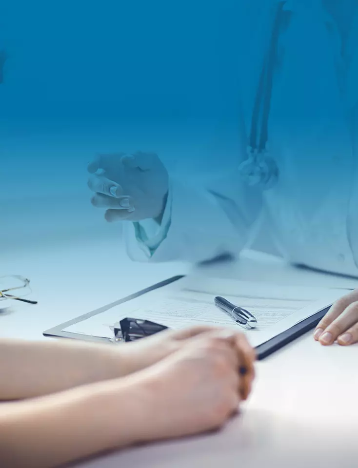 A doctor is sitting with a patient at a desk on which a document is lying.