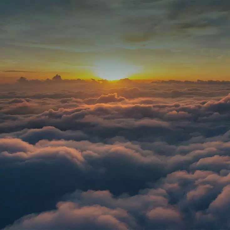 Una foto dalla prospettiva di un aereo: Un tramonto dorato con un'ampia copertura nuvolosa.