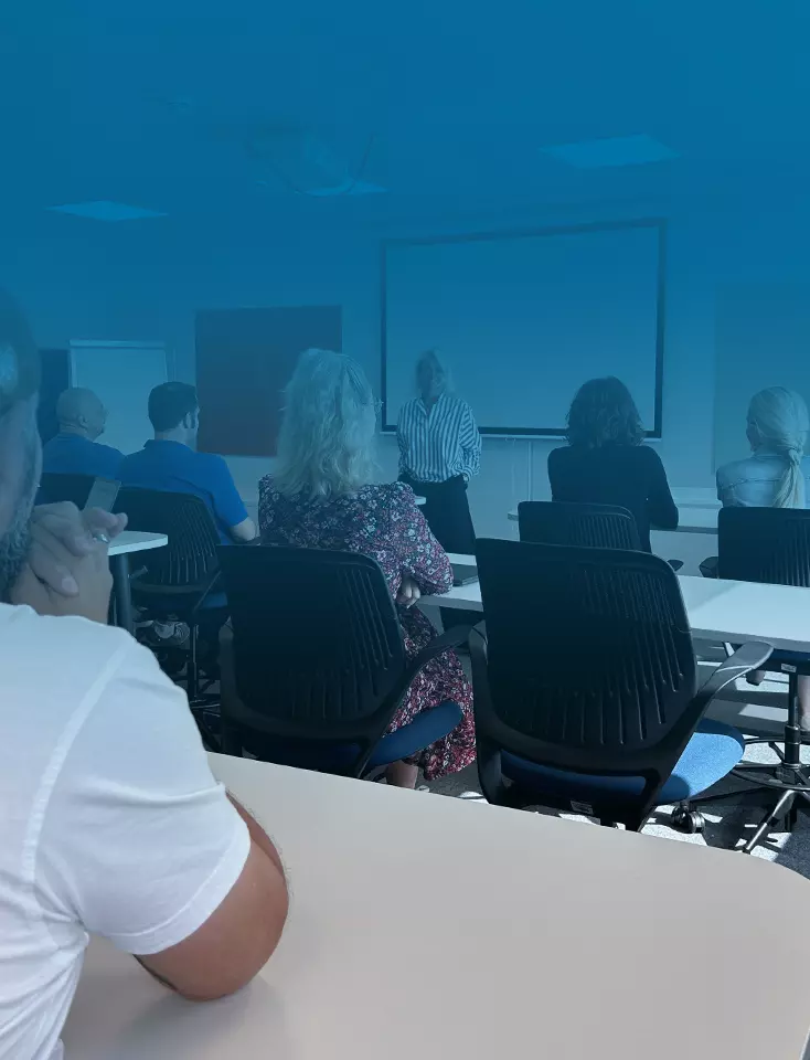 A group of people in a room during a presentation by a woman.